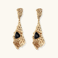 Gold-toned geometric mesh earrings with black triangular resin stones and fringe detail on neutral background