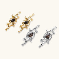 Gold-toned abstract dangle earrings with flowing cutout design and dark resin center accents on white background.