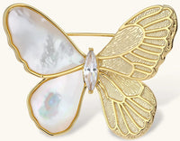 Gold-plated butterfly brooch with mother-of-pearl left wings, engraved gold right wings, and central zirconia crystal on cream background.