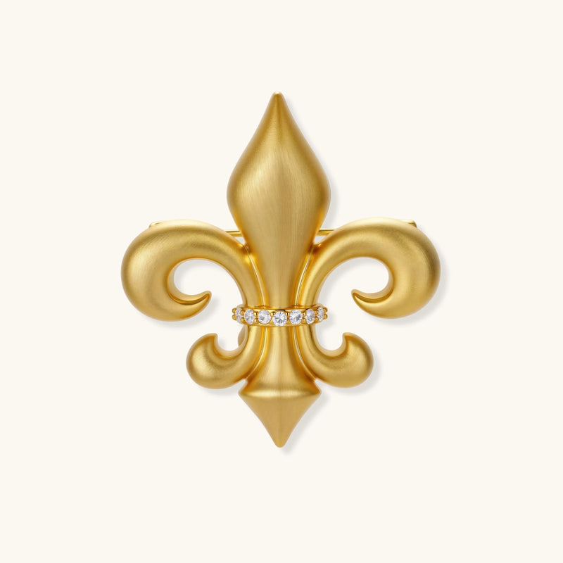 Ornate gold-plated fleur-de-lis brooch with crystal band detail on white background, showing brushed metal finish.