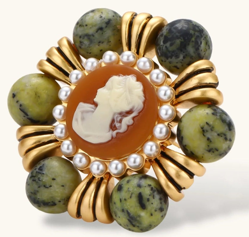 Ornate gold-plated brooch with central cameo, radiating spokes, pearl border, and green marbled natural stones on white background.