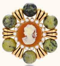 Ornate gold-plated brooch with central cameo, radiating spokes, pearl border, and green marbled natural stones on white background.