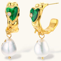 Gold-plated drop earrings with green heart charms and baroque freshwater pearls on neutral background.