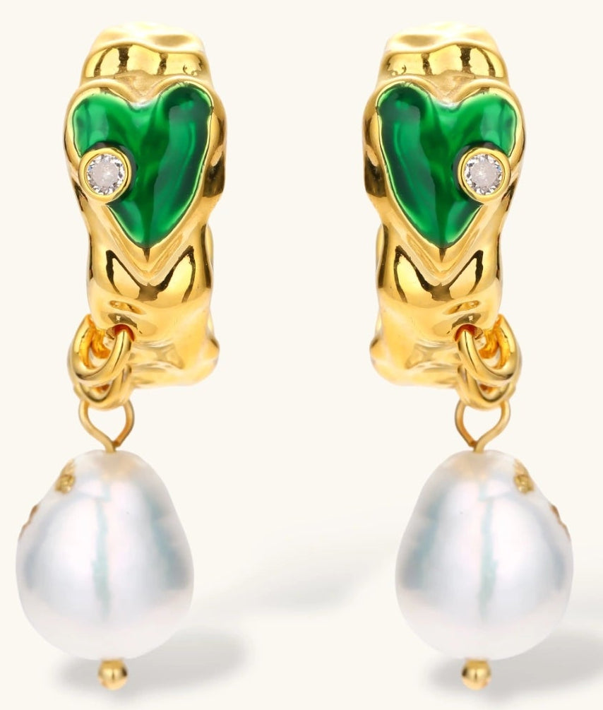 Gold-plated drop earrings with green heart charms and baroque freshwater pearls on neutral background.