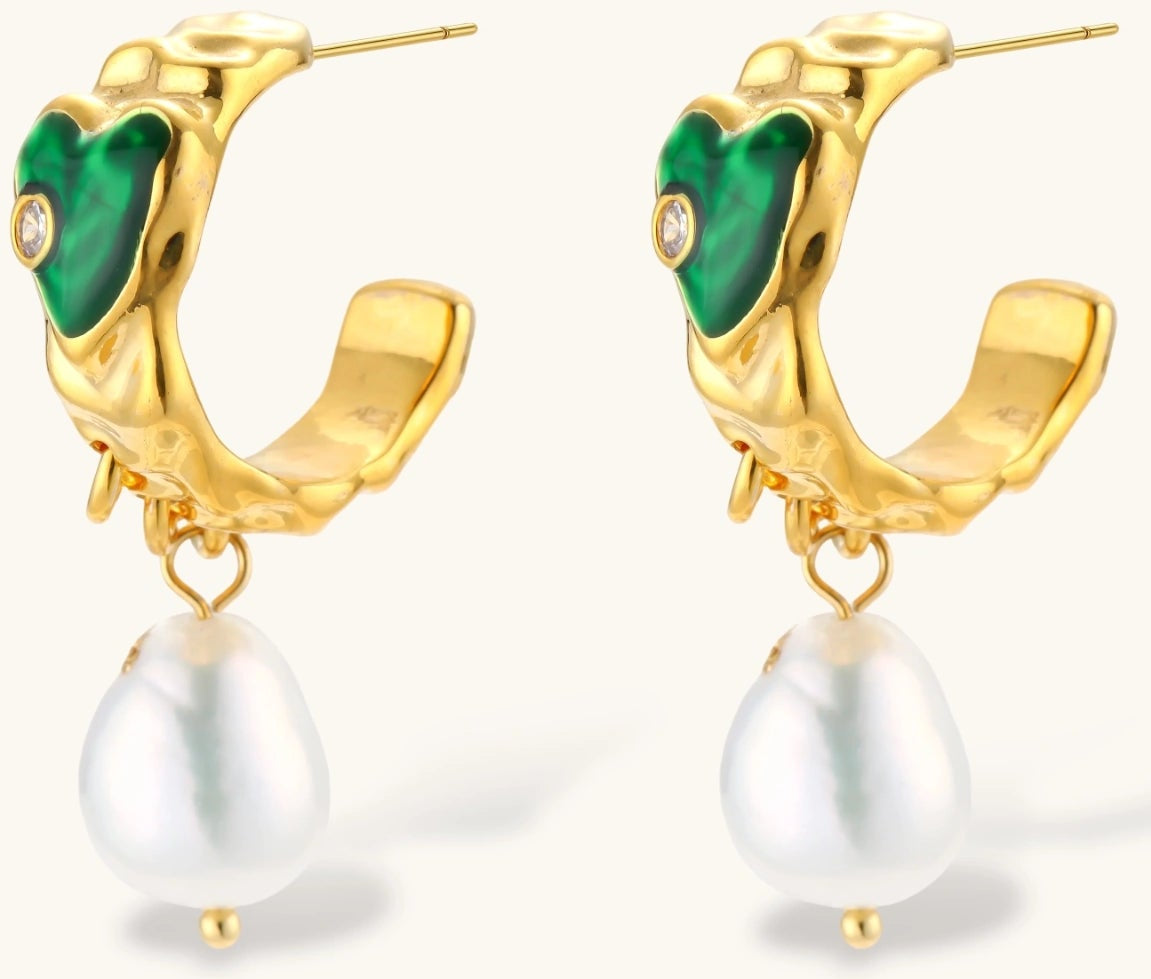 Gold-plated drop earrings with green heart charms and baroque freshwater pearls on neutral background.