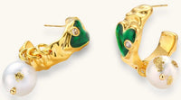 Gold-plated drop earrings with green heart charms and baroque freshwater pearls on neutral background.