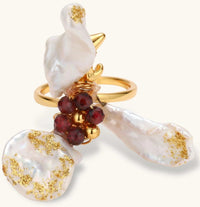Adjustable gold-plated ring featuring clustered baroque pearls with golden inclusions and burgundy gemstones in sculptural arrangement.