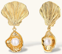 Gold shell-shaped drop earrings with scallop tops and oyster bottoms featuring round freshwater pearls on white background.
