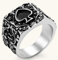 Silver-tone 316L stainless steel signet ring with black enamel spade motif and intricate floral scrollwork relief detail.