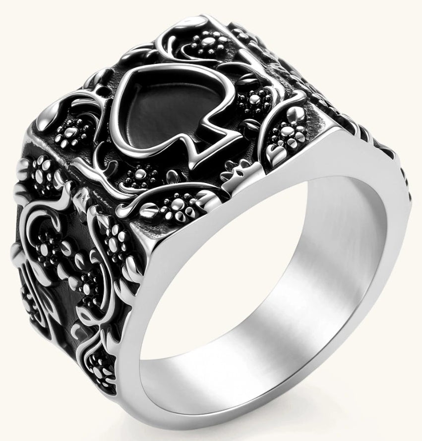 Silver-tone 316L stainless steel signet ring with black enamel spade motif and intricate floral scrollwork relief detail.
