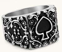 Silver-tone 316L stainless steel signet ring with black enamel spade motif and intricate floral scrollwork relief detail.