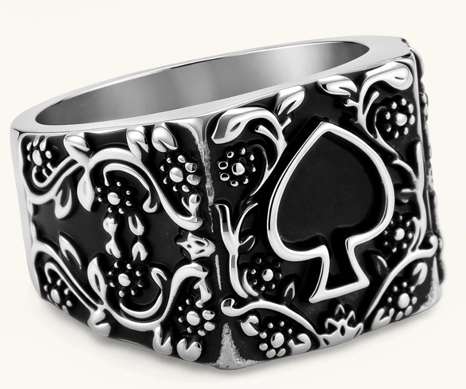 Silver-tone 316L stainless steel signet ring with black enamel spade motif and intricate floral scrollwork relief detail.