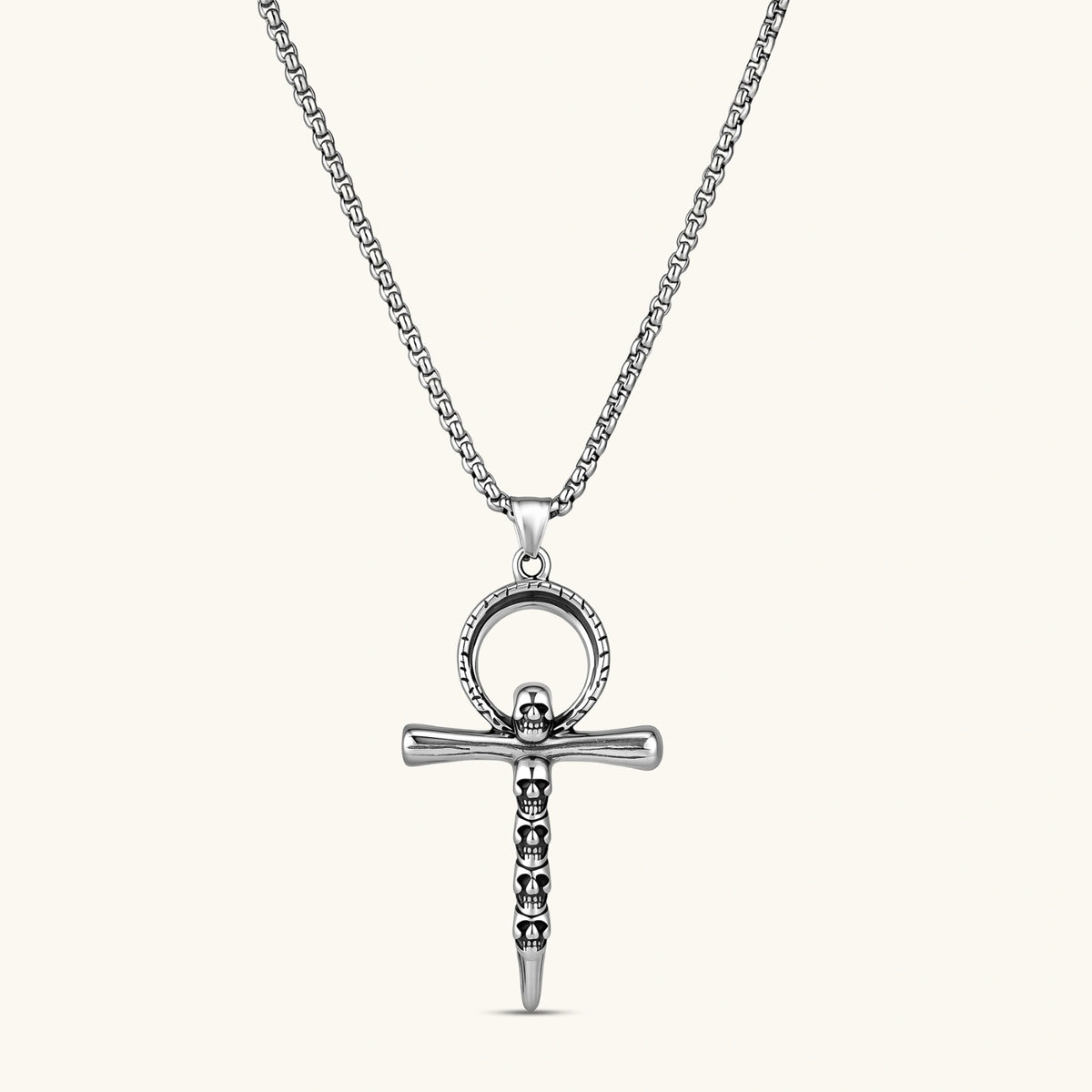 Silver stainless steel ankh pendant with skull motifs on vertical bar and textured ring top, on a box chain necklace.