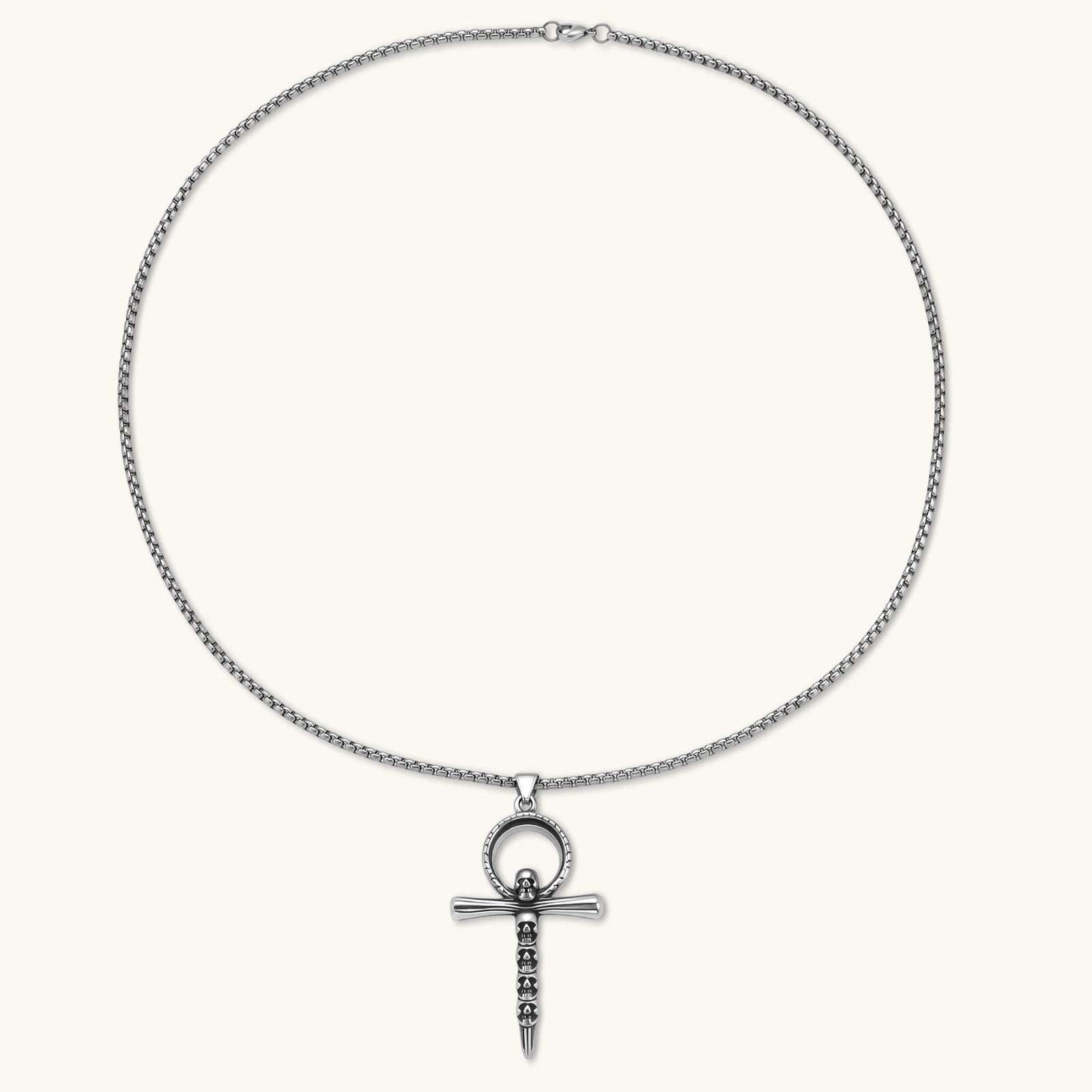 Silver stainless steel ankh pendant with skull motifs on vertical bar and textured ring top, on a box chain necklace.
