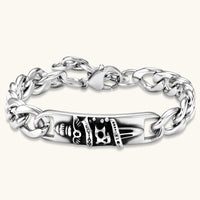 Silver 316L stainless steel Cuban chain bracelet with blackened skull and crown ID bar centerpiece, lobster clasp closure.