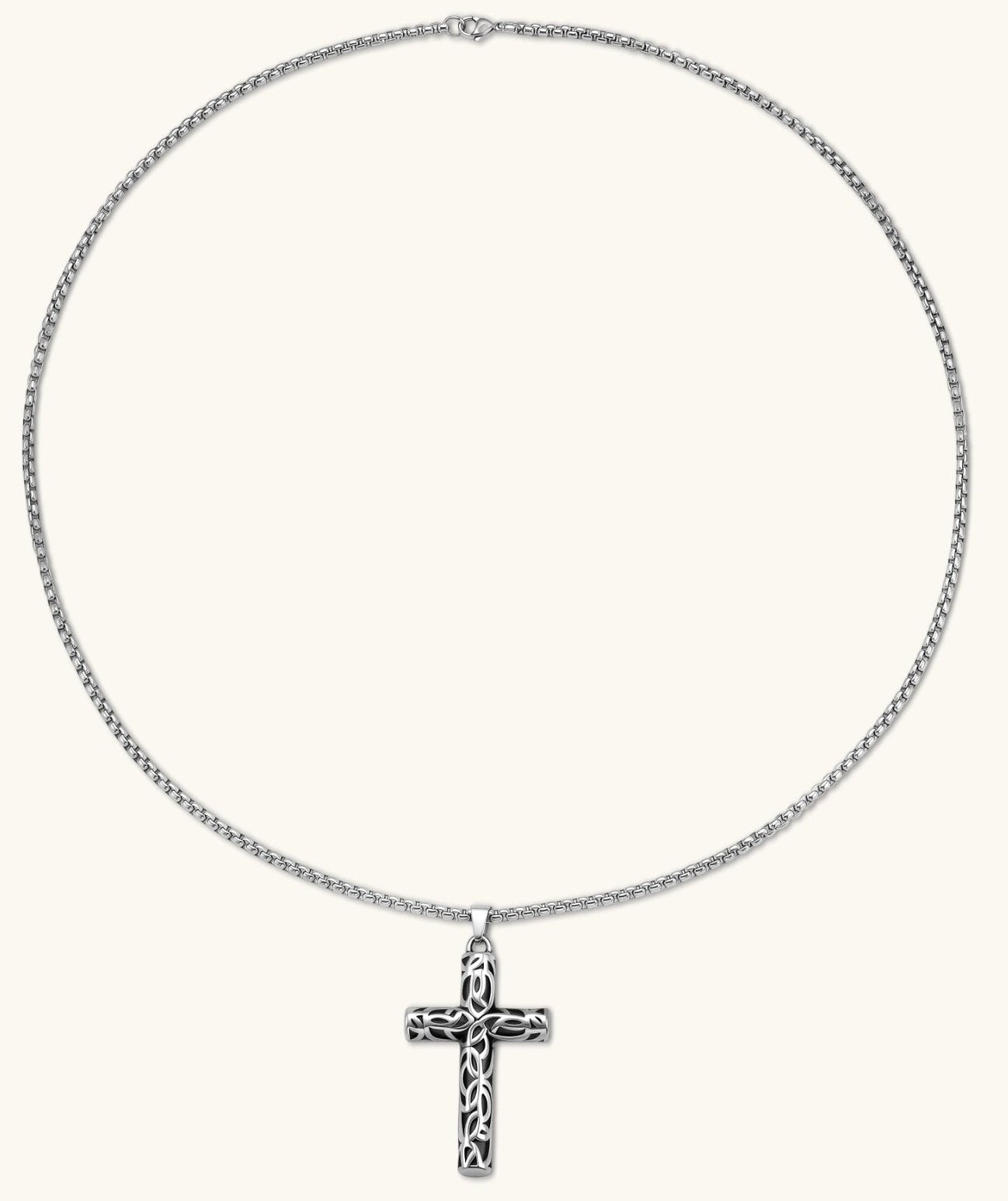 Silver stainless steel Celtic cross pendant with filigree vine pattern on a box chain, against a cream background.