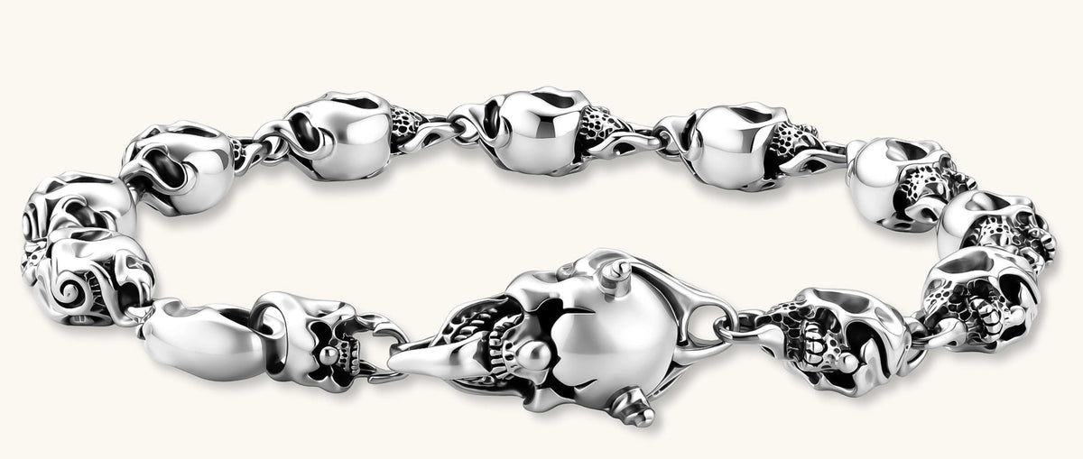 Sterling silver bracelet with linked skull motifs, decorative scroll engravings, and a large skull lobster-claw clasp.