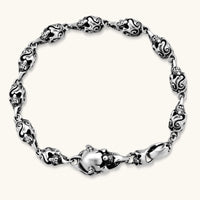 Sterling silver bracelet with linked skull motifs, decorative scroll engravings, and a large skull lobster-claw clasp.